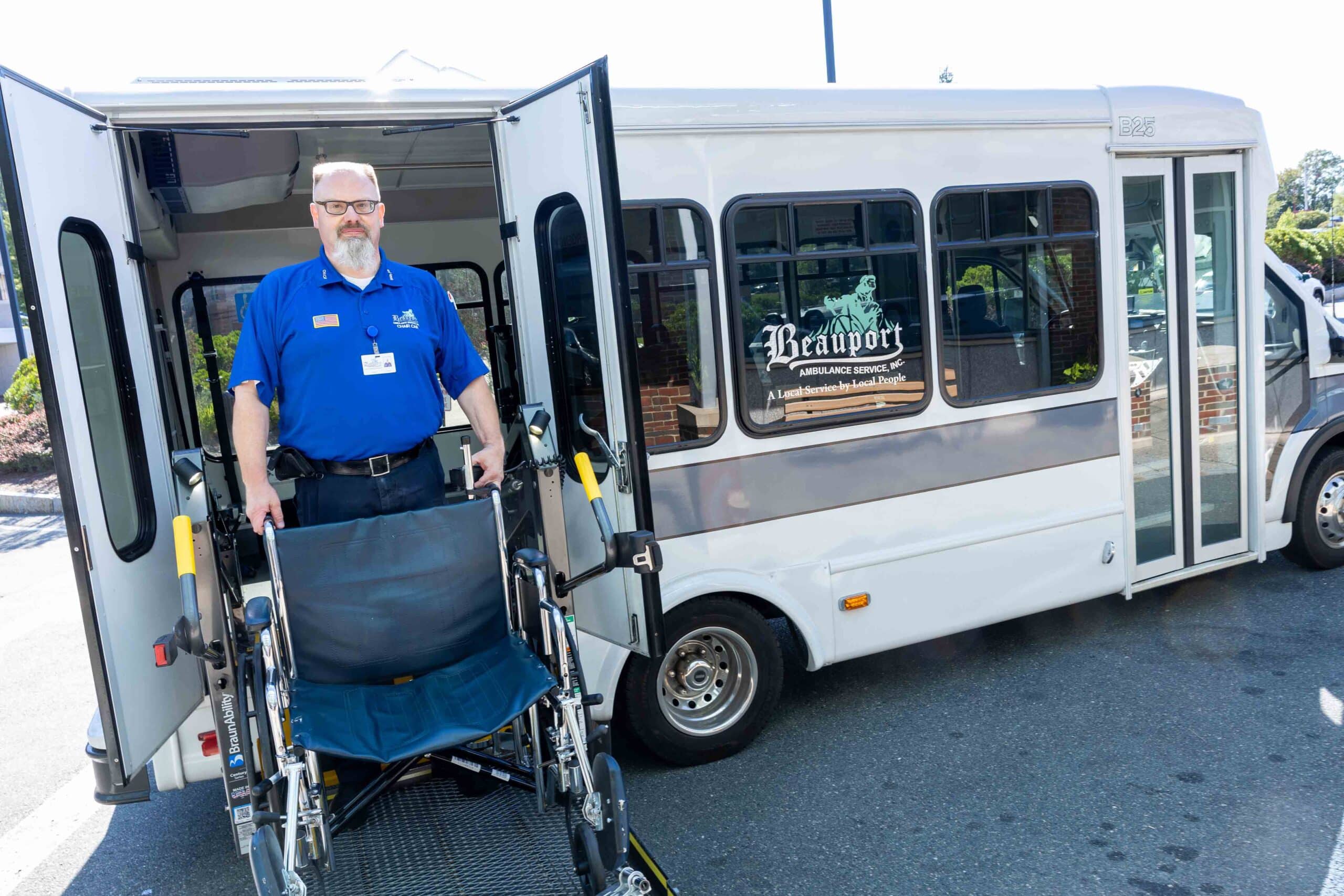 A staff member holds a wheelchair next to a company bus.